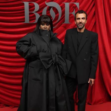 Cédric Charbit on a red carpet beside another guest, standing in front of a red curtain backdrop marked BoF