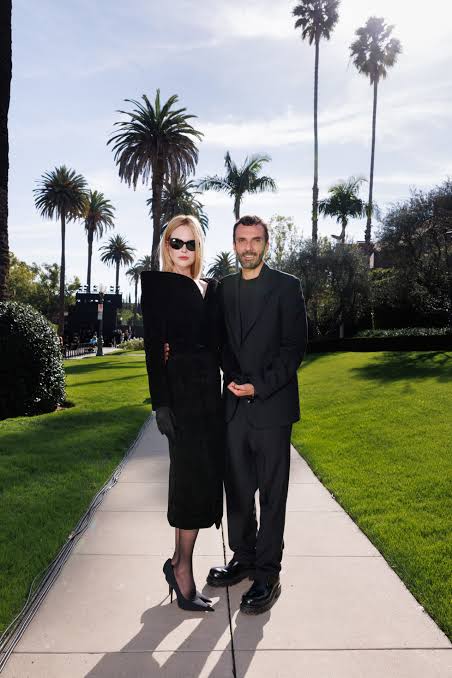 Cédric Charbit standing outdoors beside a guest on a garden path with tall palm trees and a clear sky behind