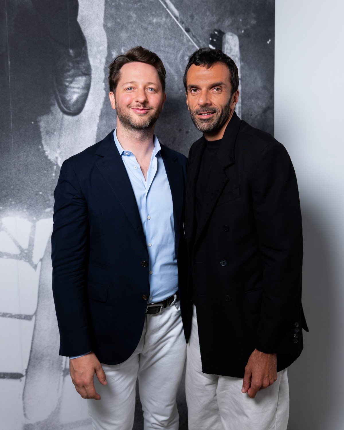 Cédric Charbit standing beside Derek Blasberg in front of a large black and white artwork at a Gagosian gallery event in Paris