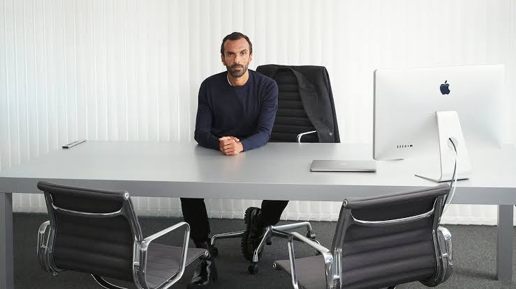 Cédric Charbit seated at a long table in a minimal office, with a computer and two chairs opposite